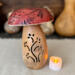 Decorative mushroom made from dried gourds. A berry color top has dragonfly artwork. The bottom as a carved vine that lights with a candle. 